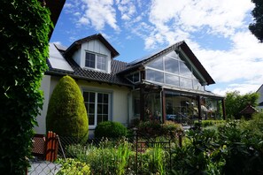 Een woning met een grote glazen conservatorium, een verzorgde tuin en een traditionele bouwstijl.