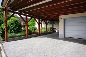 A covered outdoor area with a garage, wooden beams, and a paved floor. - Vacation apartment with conservatory, in a quiet location with outdoor seating for 4 pers. (Dürrwangen)