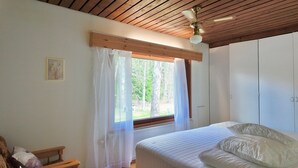 Ein Schlafzimmer mit Bett, einem Fenster mit Vorhängen, einem Deckenventilator und einem Holzkopfschild.