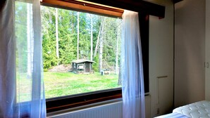 Ein Schlafzimmer mit Fensterblick auf einen Wald, eine kleine Gartenhütte und eine Heizung.