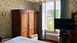 Ein Schlafzimmer mit Holzschrank, Fernseher, Heizkörper und einem fenster mit Vorhängen.