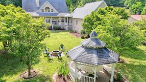 Uma casa grande com varanda coberta, um gazebo e uma lareira no quintal.