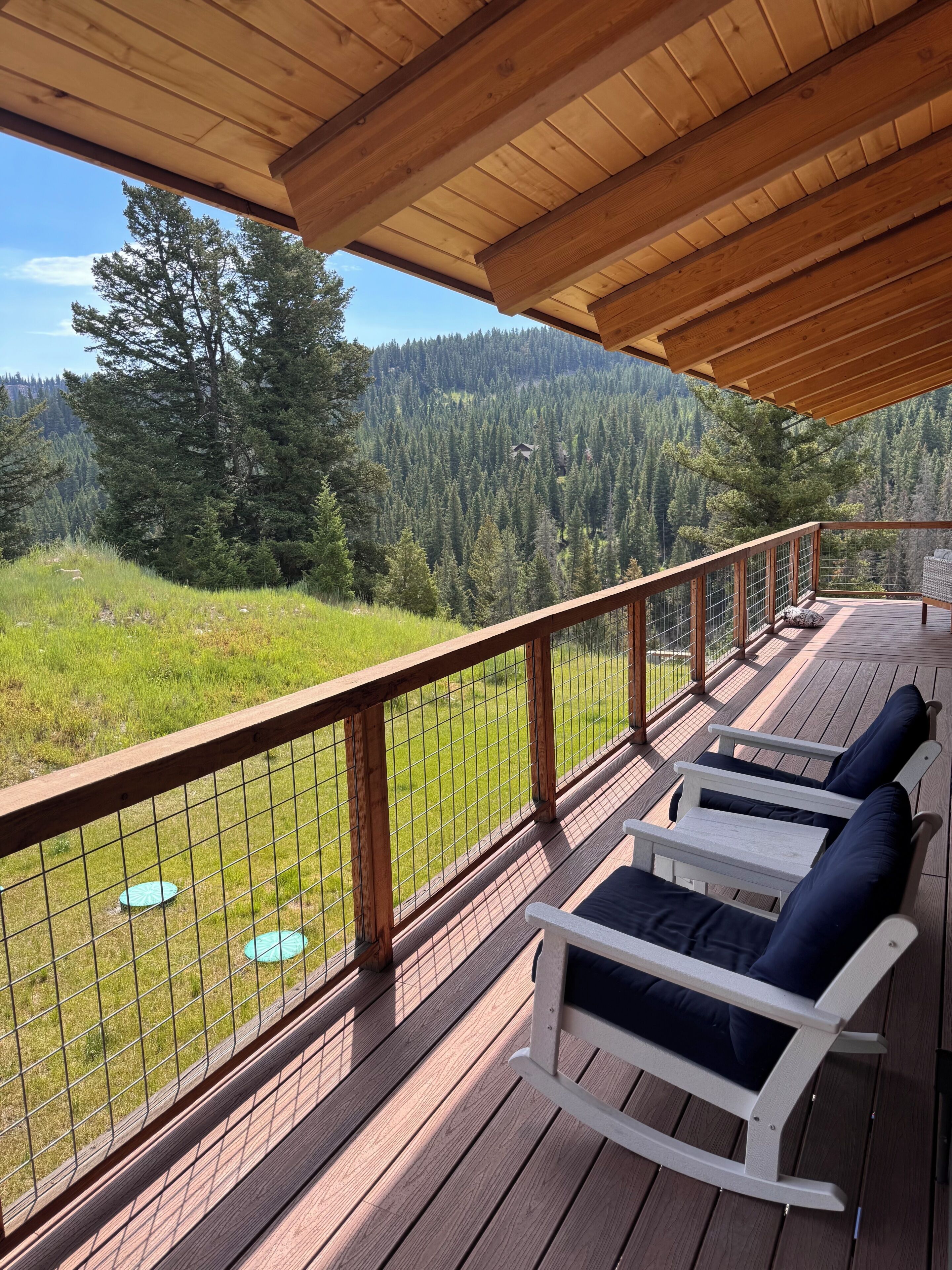 A wooden deck with a railing, outdoor seating, and a view of a forested mountain.