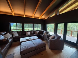 Ein modernes Wohnzimmer mit einer Eckcouch, einem Couchtisch und großen Fenstern mit Blick auf eine Terrasse und Grünflächen.