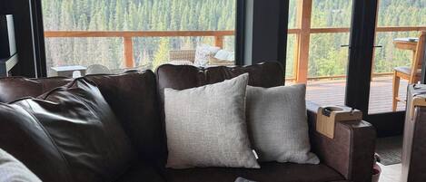 Een moderne woonkamer met een groot raam met uitzicht op een bebost berglandschap.