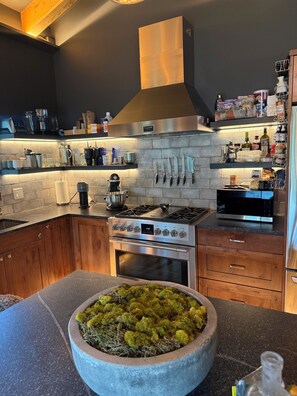 Eine moderne Küche mit Einbauherd, Backofen und einer großen Kochinsel mit Moosdekoration.