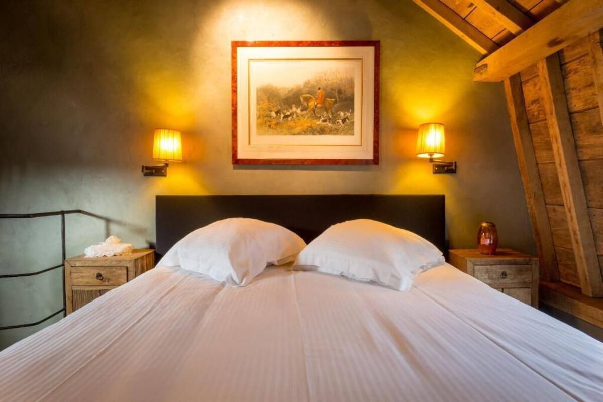 A bed with white linens, two bedside tables, a framed picture on the wall, and wall-mounted lamps.