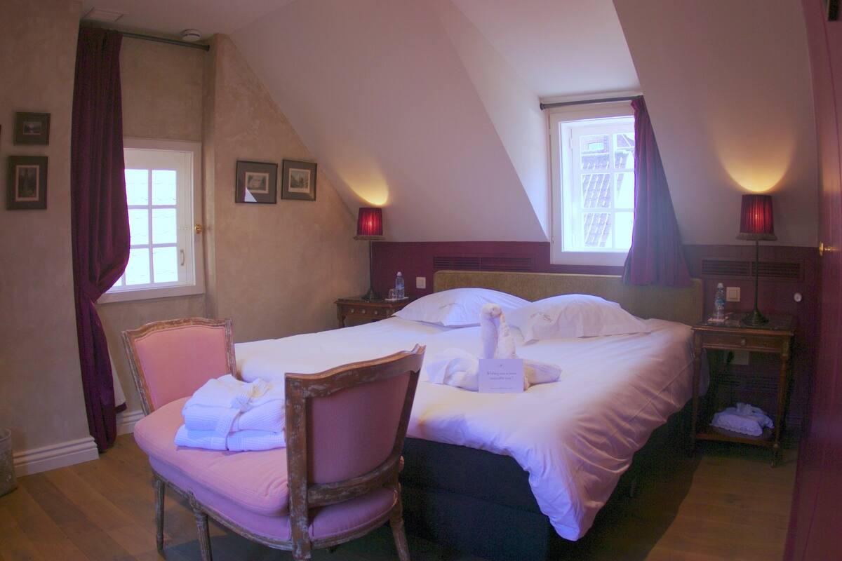 A hotel room with a bed, a chair, a nightstand, a lamp, and a window with curtains.