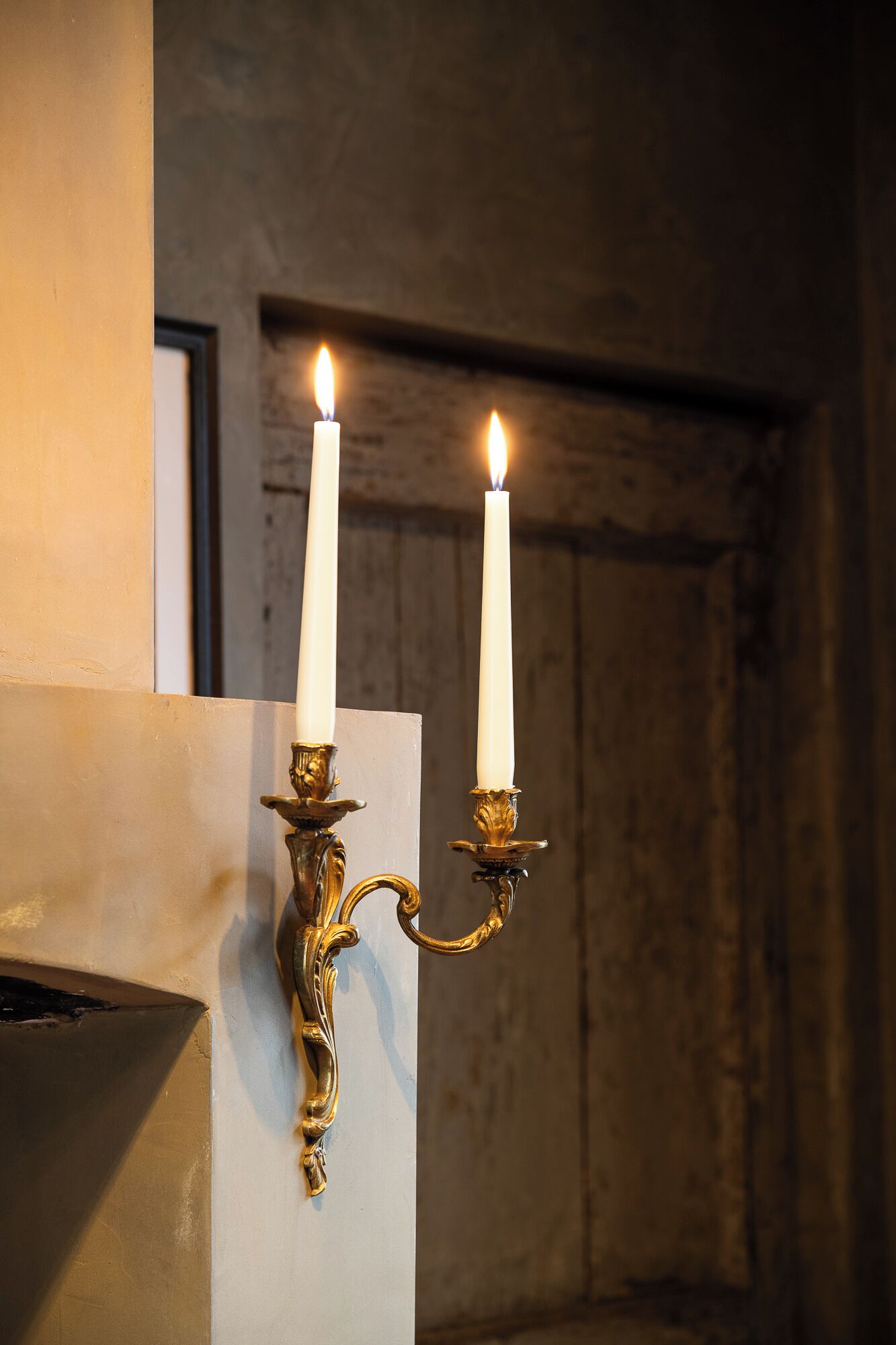 Two lit candles on ornate wall sconces.