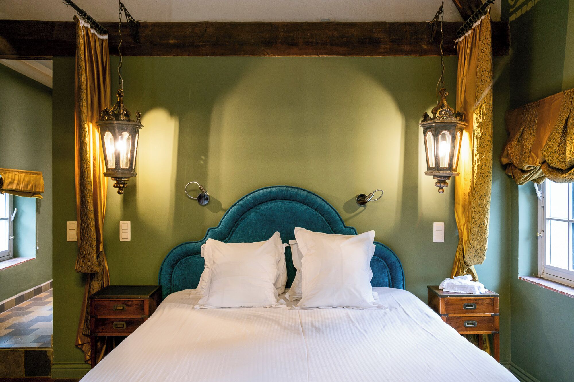 Un lit avec une tête de lit de couleur turquoise, deux appliques murales et une table de chevet en bois dotée de tiroirs.