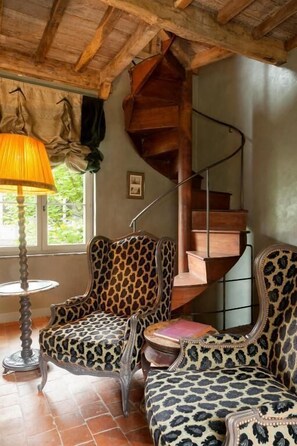 A room with a spiral staircase, leopard-print upholstered chairs, a round table, and a lamp.