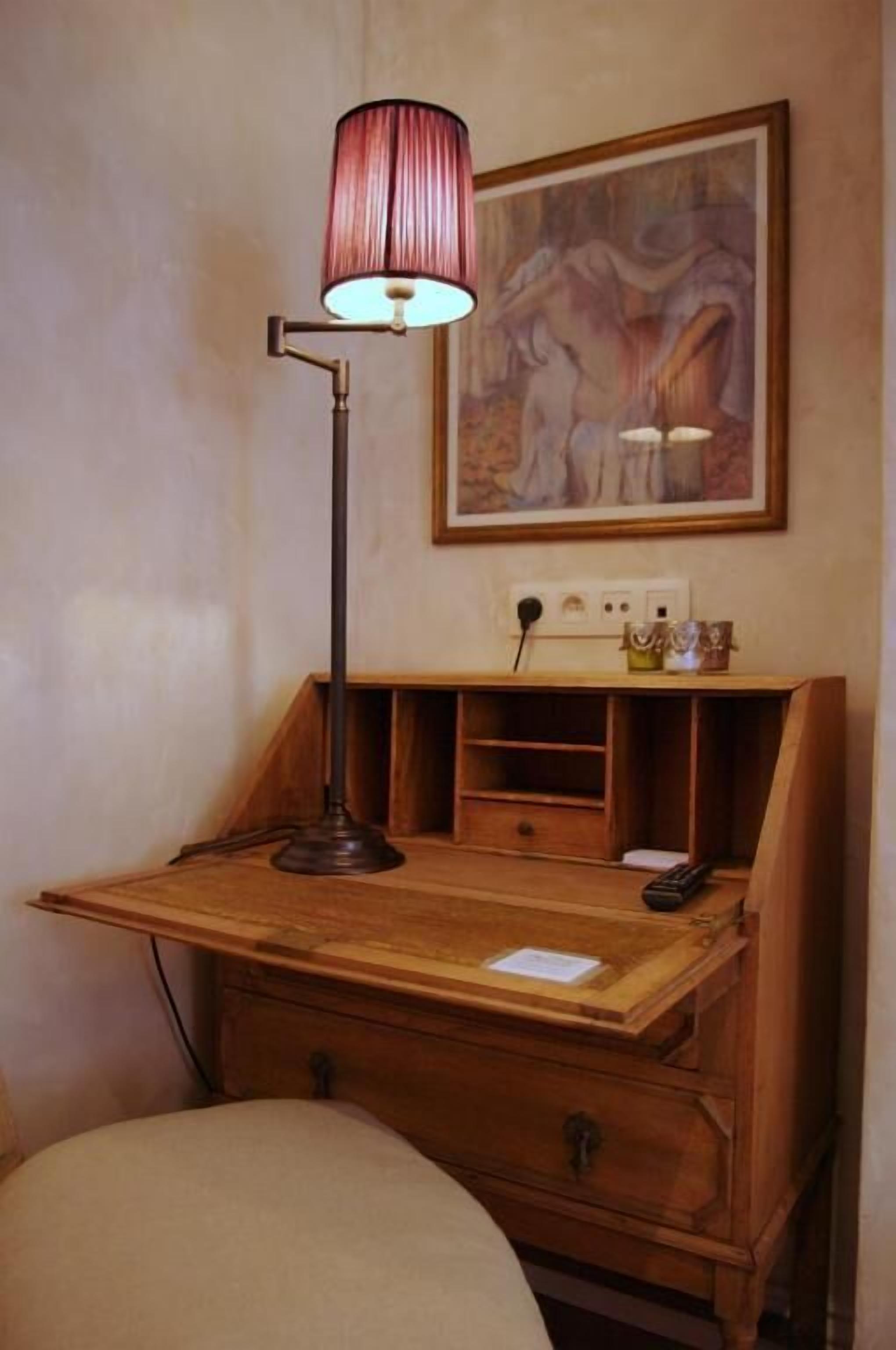 Un bureau en bois, une lampe, un tableau accroché au mur et une prise de courant.