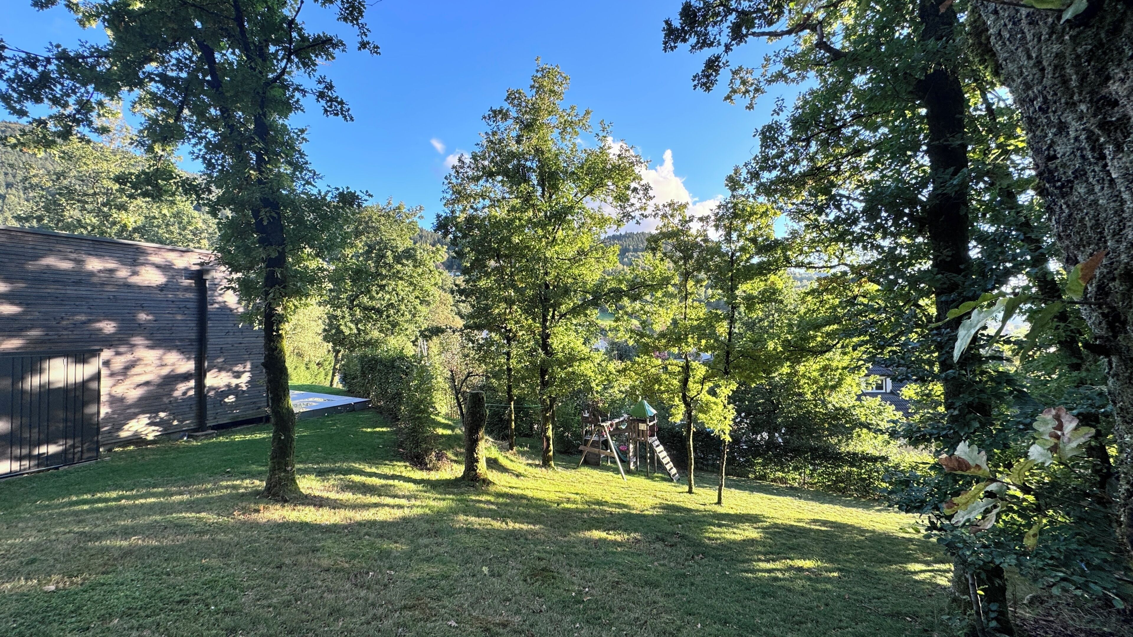 Ein Garten mit einer Holzterrasse, einem Trampolin und einer Spielanlage.