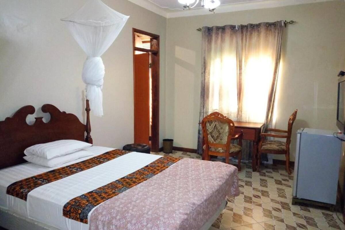 Un dormitorio con cama, mesita de noche, silla, escritorio y ventana con cortinas.
