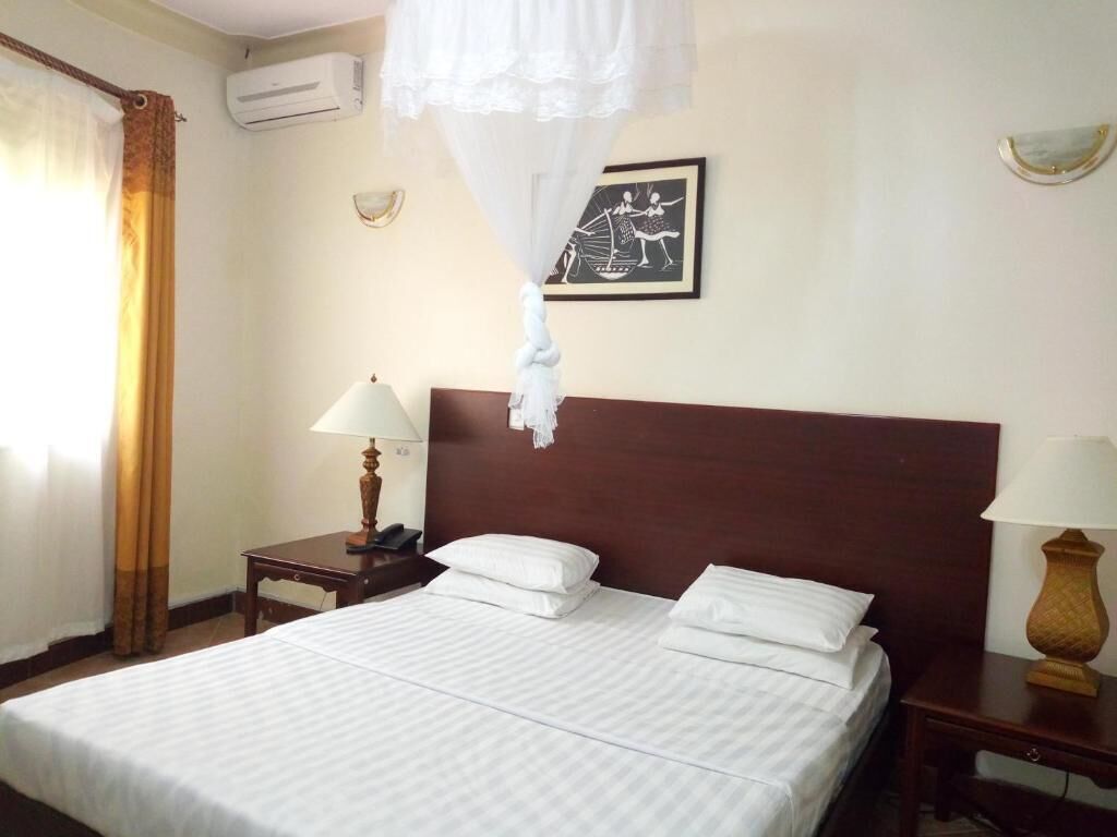 Habitación de hotel con cama, dos mesitas de noche, aire acondicionado de pared, un cuadro enmarco y una ventana con cortinas.