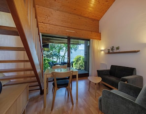Ein modernes Interieur mit einer Holztreppe, einer Essecke mit Tisch und Stühlen, einer Couch und Blick ins Grüne.