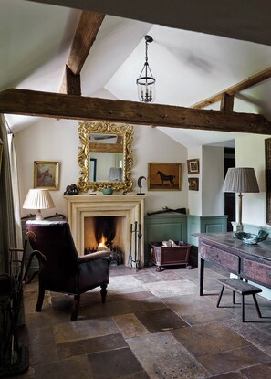A rustic room with exposed wooden beams, a fireplace, a mirror, and a horse-themed painting.