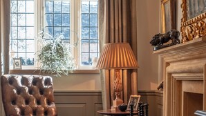Une pièce avec un fauteuil en cuir, une lampe, une cheminée et une fenêtre avec des rideaux.