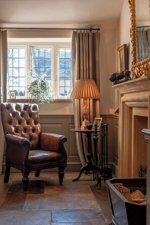A room with a leather armchair, a lamp, a fireplace, and a window with curtains.