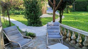 Een terras met stenen vloer, twee loungestoelen, een kleine tafel en een pergola met lantaarn.