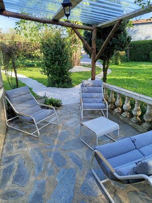 Eine Terrasse mit Steinplatten, zwei Liegestühle, ein kleiner Tisch und eine Pergola mit einer Laterne.