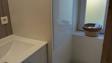 A compact bathroom with a white sink, a toilet, and a window with a basket on the sill.