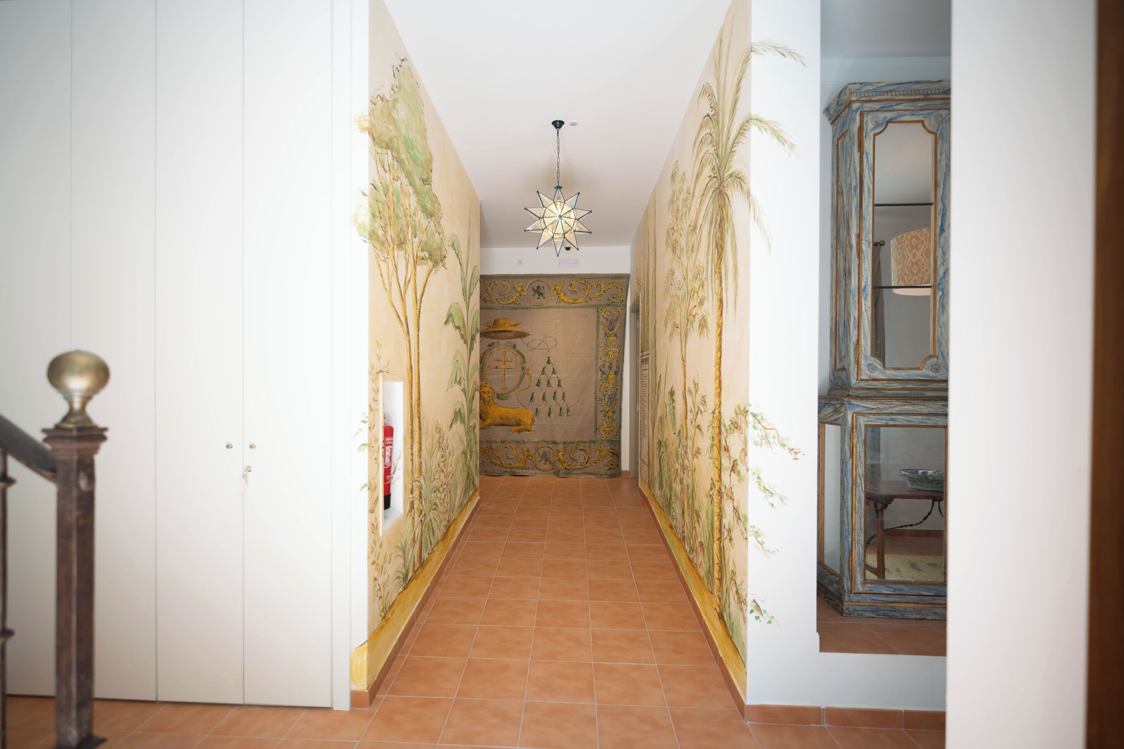 Un pasillo con suelo de baldosas, una escalera a la izquierda y una pared con un mural decorativo.