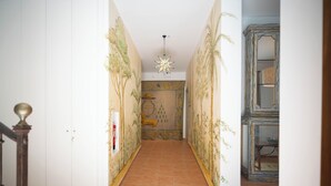 Un pasillo con suelo de baldosas, una escalera a la izquierda y una pared con un mural decorativo.