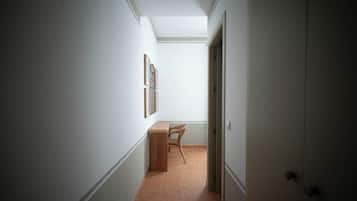 Un pasillo con una puerta a la derecha, una silla y un estante en la pared con objetos enmarcados.