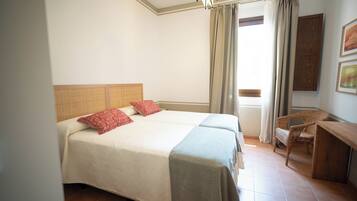 Una cama doble con cabecera, dos almohadas, una mesita de noche, una silla y una ventana con cortinas.
