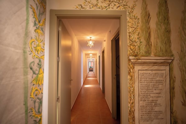 A hallway with a star-shaped light fixture, a door on the left, and a wall with a decorative panel on the right. - Posada Santa Paula (Seville)