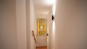 Un pasillo estrecho con paredes blancas, un marco de puerta de madera y una obra de arte colgada.