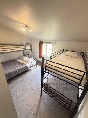 Une chambre de dortoir avec deux lits superposés, une fenêtre avec des rideaux et un luminaire au plafond.