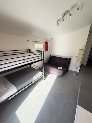 A room with a bunk bed, a sofa, a window with curtains, and a ceiling light fixture.