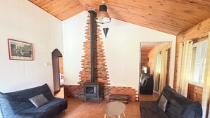 A cozy room with a brick fireplace, two black sofas, a small round table, and wooden ceiling beams. - Chalet Douglas - 30 People (Châtillon-Saint-Jean)