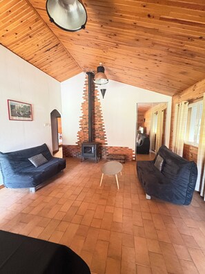 A cozy room with a brick fireplace, two black sofas, a small round table, and wooden ceiling beams.