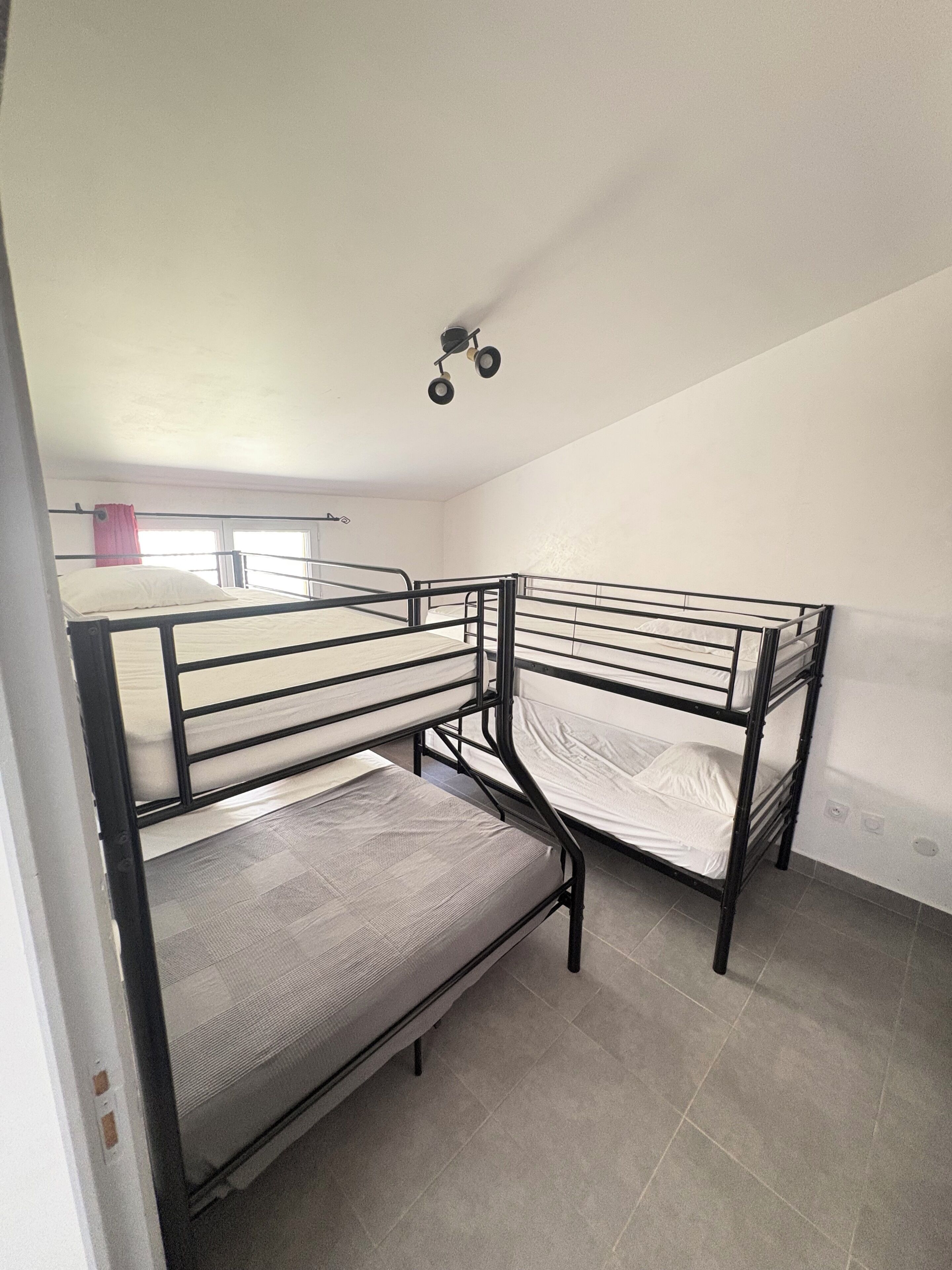 Une chambre de dortoir avec des lits superposés, une fenêtre avec des rideaux et un luminaire au plafond.