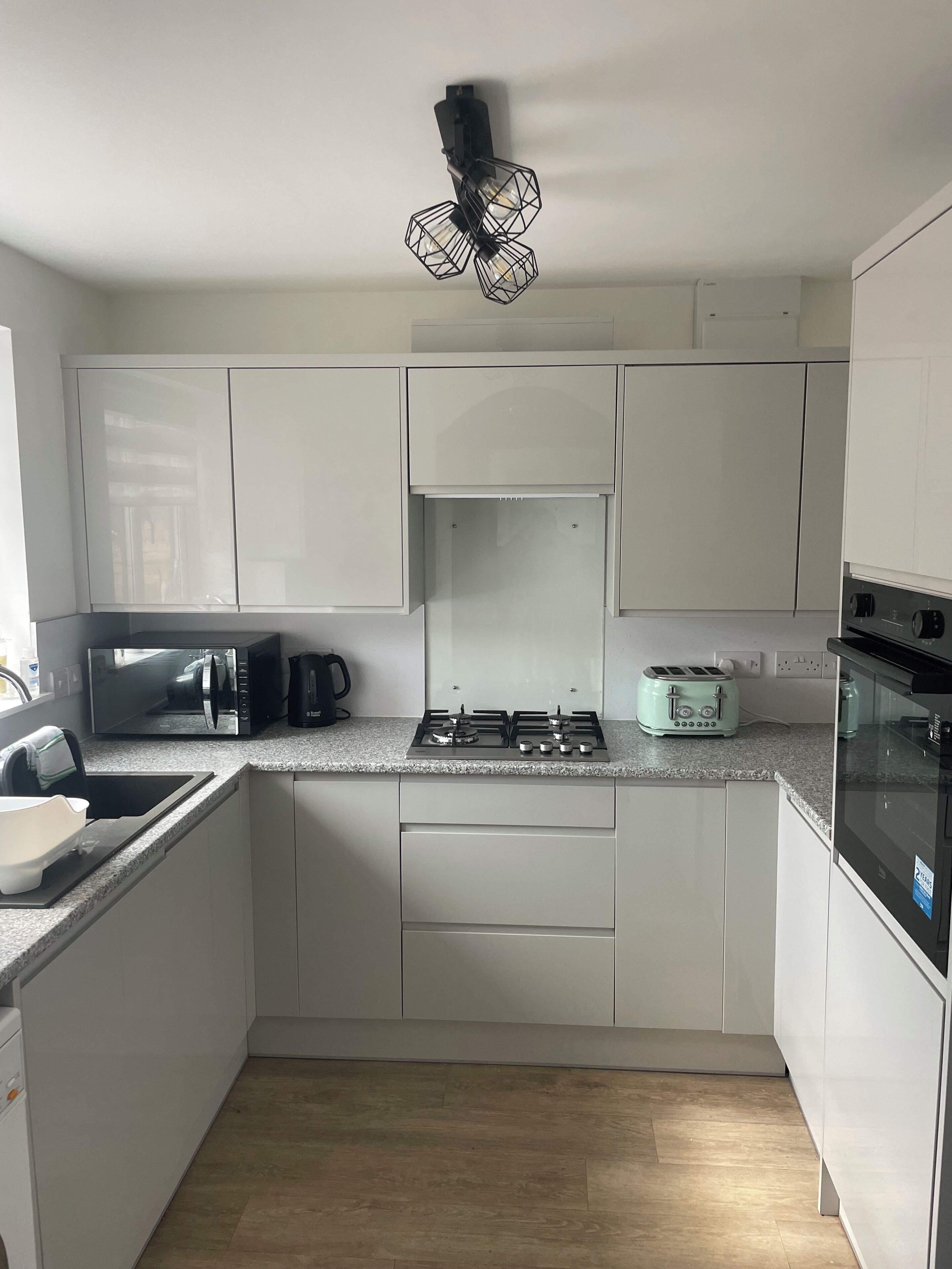 A modern kitchen with white cabinets, a microwave, a gas stove, a toaster, and a black hanging light fixture.