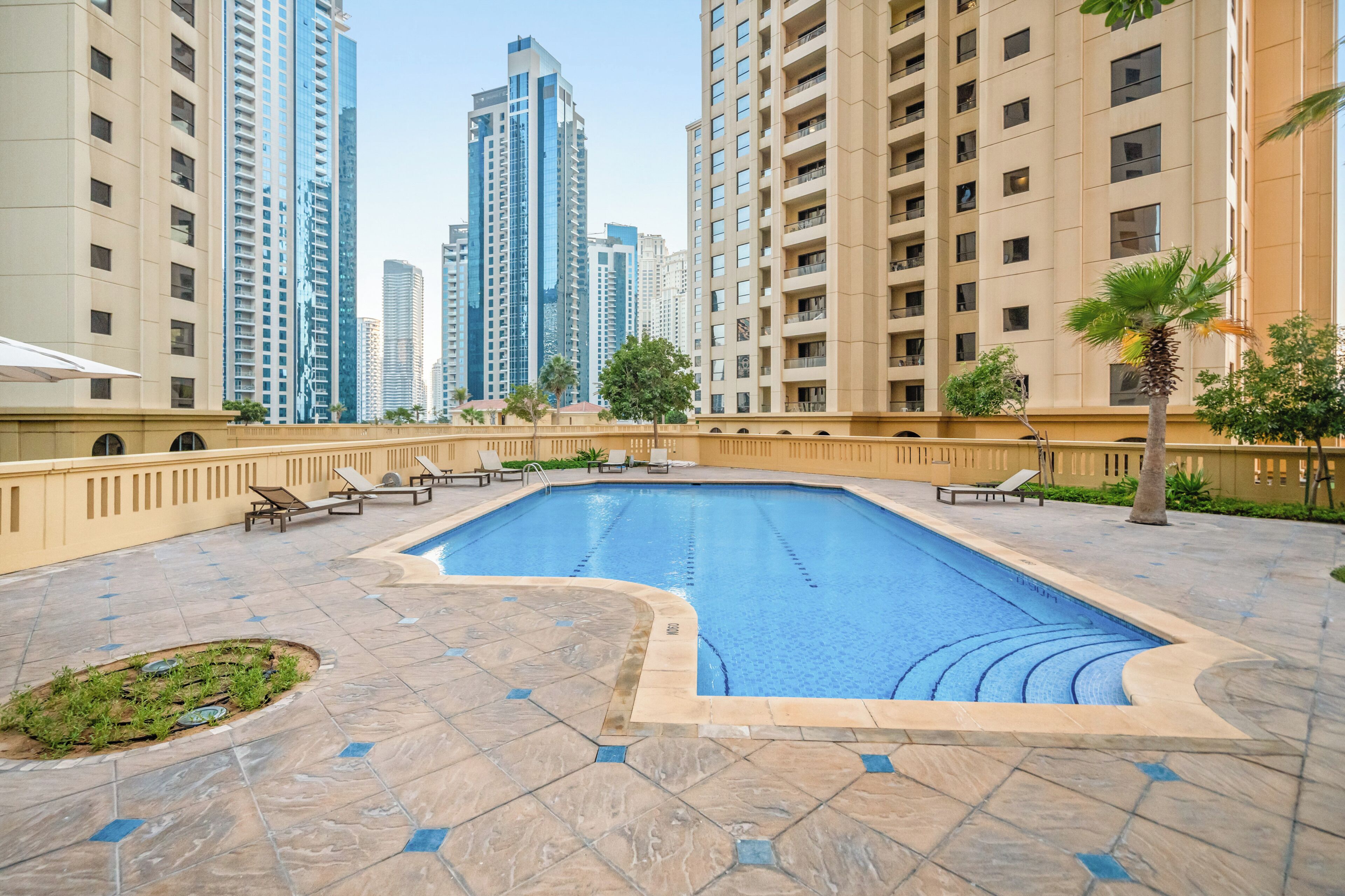 Una piscina con sillas de descanso, rodeada de edificios altos.