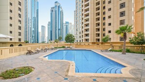 A swimming pool with lounge chairs, surrounded by high-rise buildings. - Spacious 2 Bedroom Apt in Sadaf JBR  (Dubai)