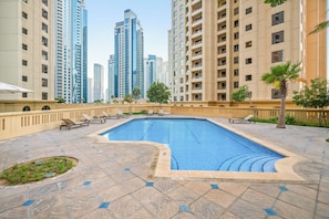 A swimming pool with lounge chairs, surrounded by high-rise buildings. - Spacious 2 Bedroom Apt in Sadaf JBR  (Dubai)