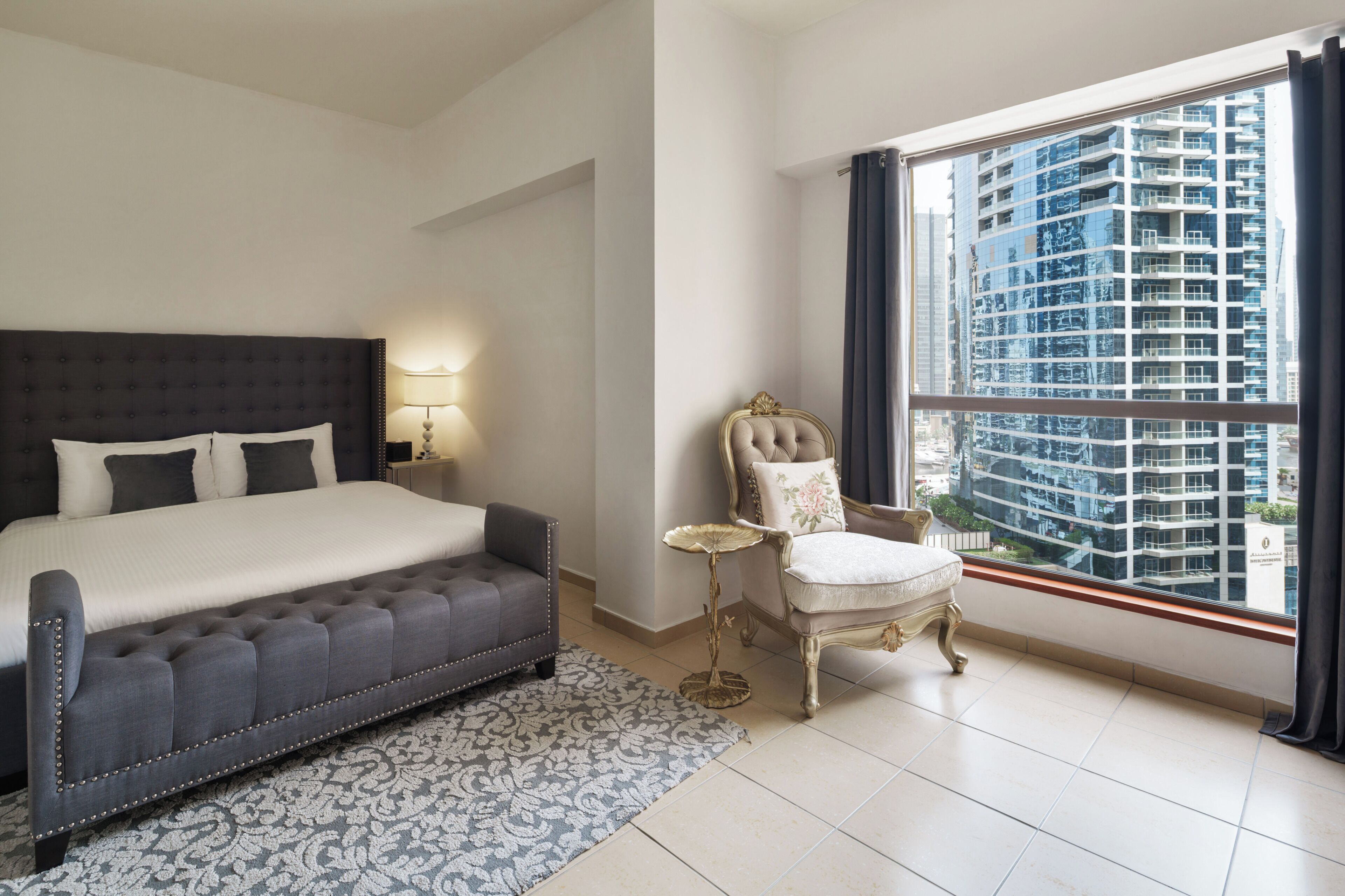 Un dormitorio con una cama grande, una mesita de noche, una silla y una ventana con vista a la ciudad.