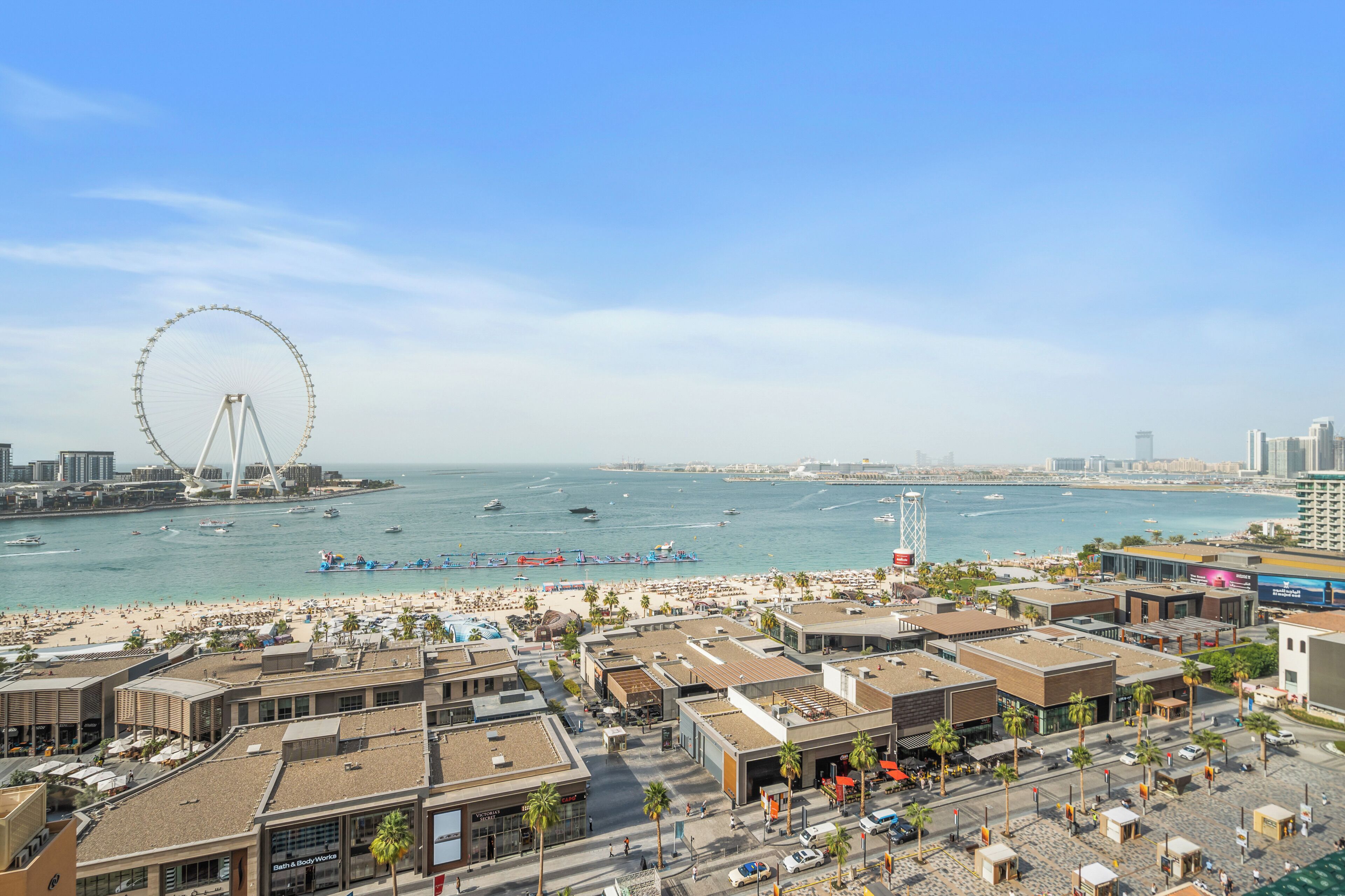 Un paisaje urbano costero con una noria destacada, frente a la playa y edificios modernos.