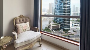 A room with a large window, a tufted chair with a floral pillow, and a gold side table. - Spacious 2 Bedroom Apt in Sadaf JBR  (Dubai)