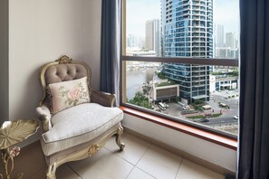 A room with a large window, a tufted chair with a floral pillow, and a gold side table. - Spacious 2 Bedroom Apt in Sadaf JBR  (Dubai)