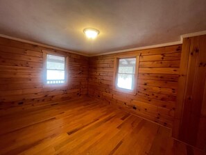 Une pièce aux murs et au plancher en bois, avec deux fenêtres et un luminaire au plafond.