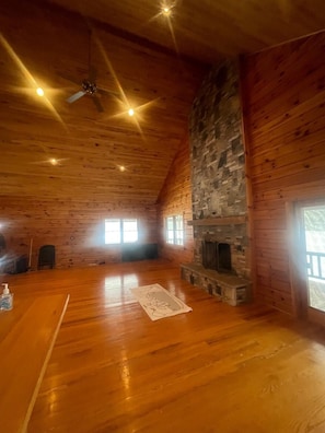 A spacious room with wooden walls, a stone fireplace, and a ceiling fan.