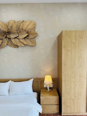 A hotel room with a bed, a nightstand with a lamp, a wooden wardrobe, and a wall decoration.