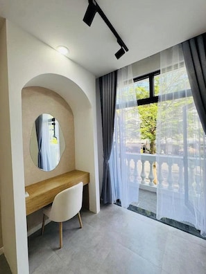 A modern room with a wooden desk, a mirror, and a large window with sheer curtains.