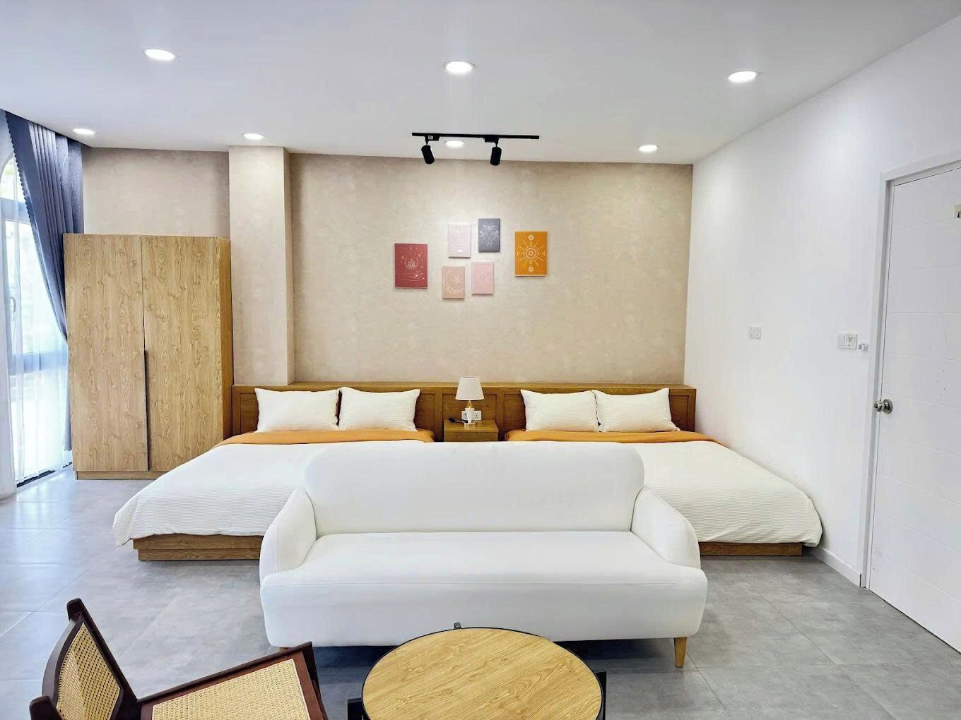 Moderni hotellihuone, jossa on suuri sänky, sohva, puinen yöpöytä ja taideteoksilla koristeltu seinä.